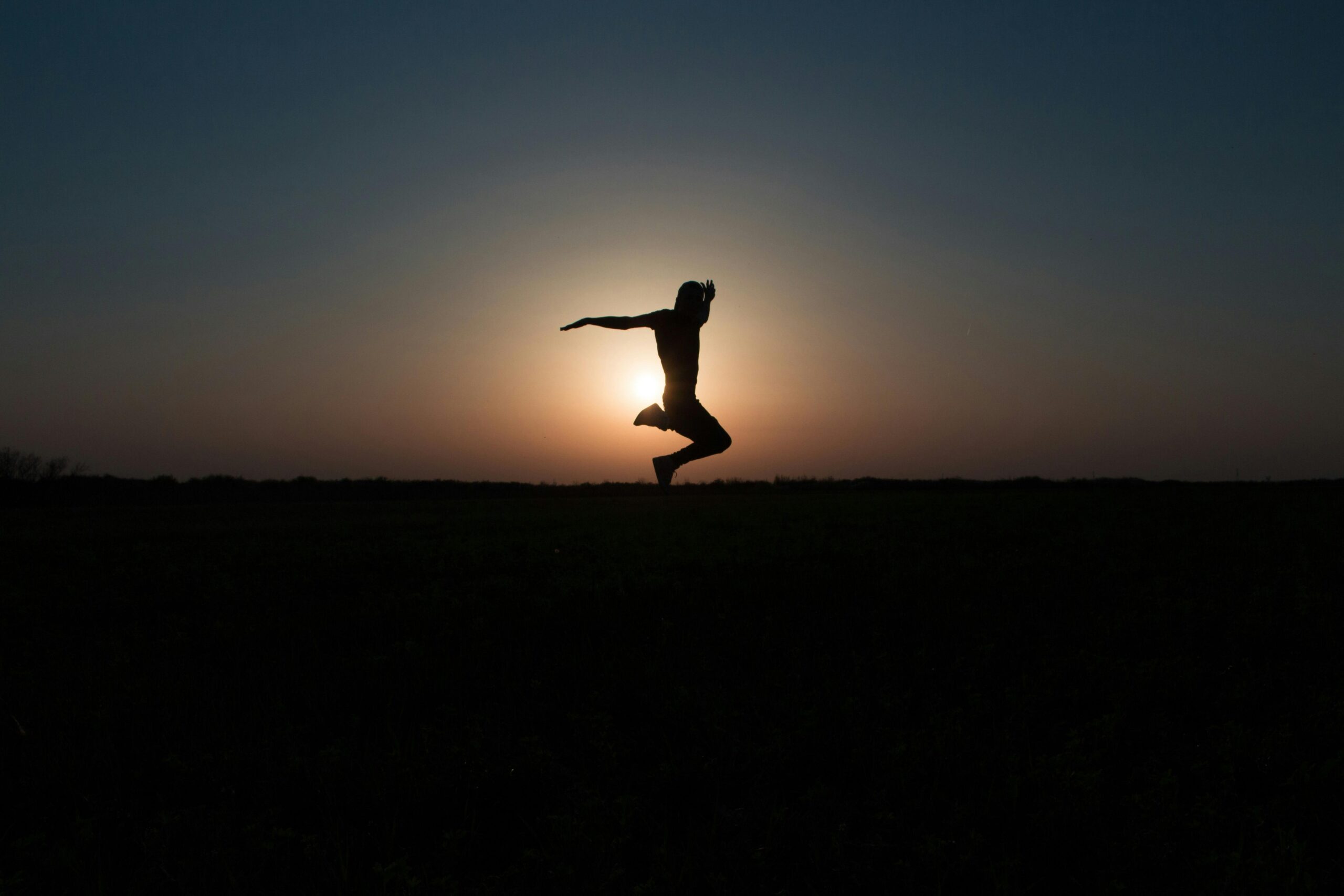 Dynamic silhouette jump against a vibrant sunset sky, symbolizing freedom and joy.