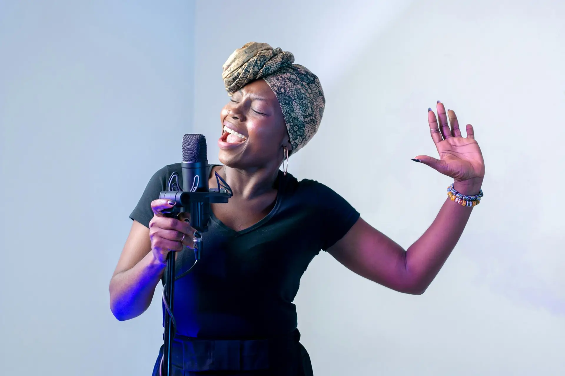 Passionate African woman singing in a music studio with a microphone and headscarf.