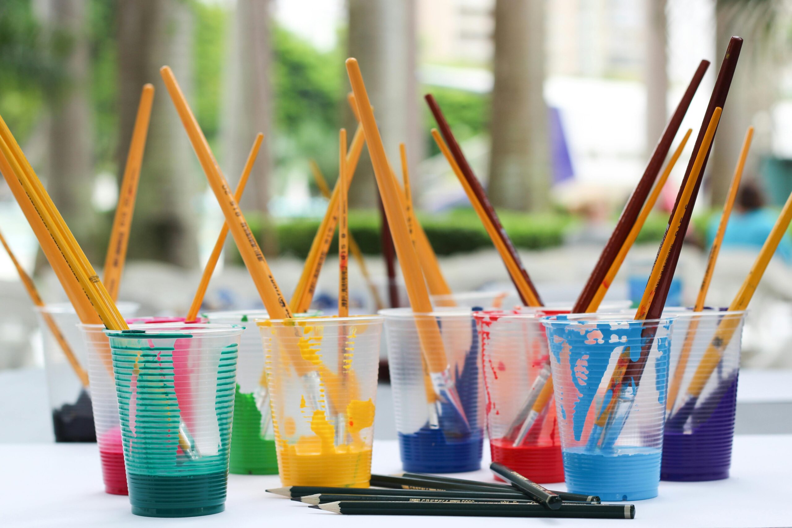 Vibrant paint brushes and pencils in plastic cups for arts and crafts.